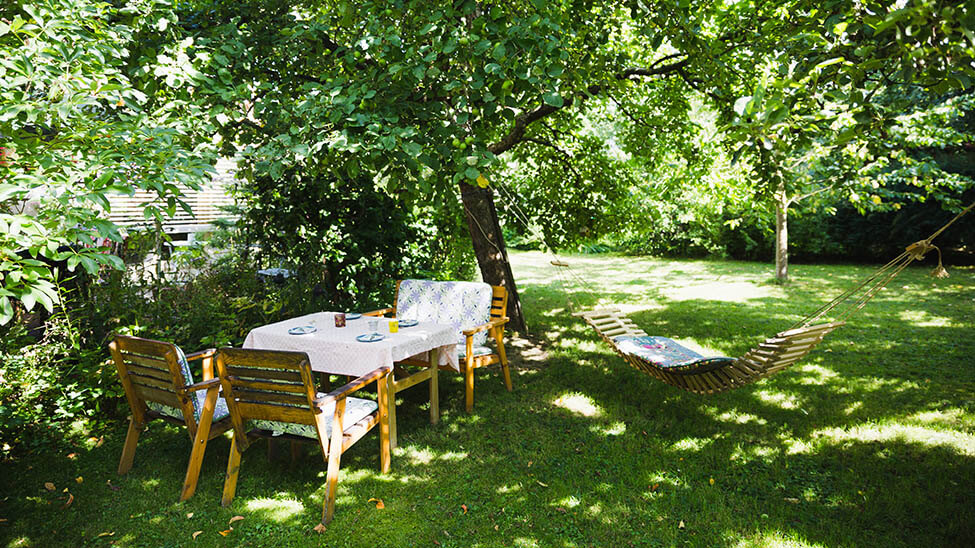 Green spacious garden where there is a table, several chairs and a hammock