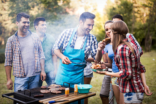 Friends relaxing outside in the garden in front of a grill talking, laughing and having fun with each other