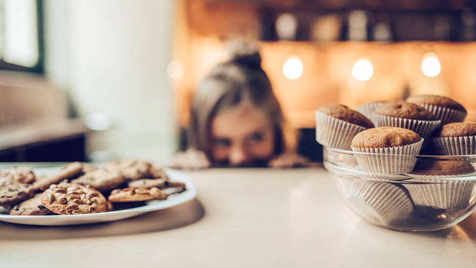 Girl looks greedily at plate and bowl full of cookies
