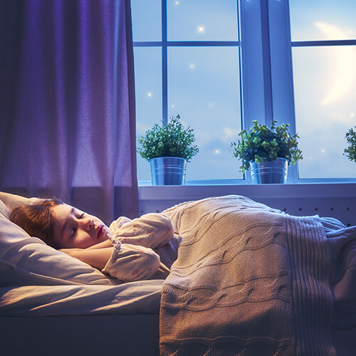 Child sleeping in bed by window in moonlight