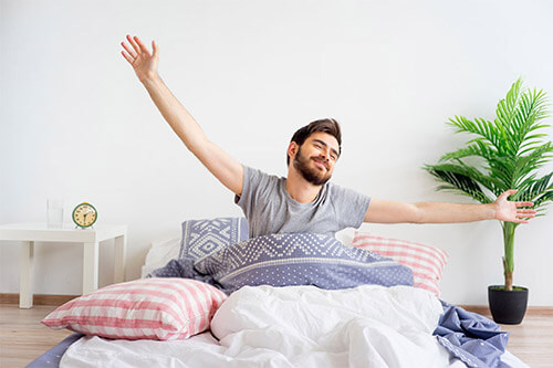 Young man stretching happily while getting up in the morning in bed