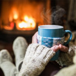 Woman in front of fireplace with warm tea and thick socks to warm cold hands and feet