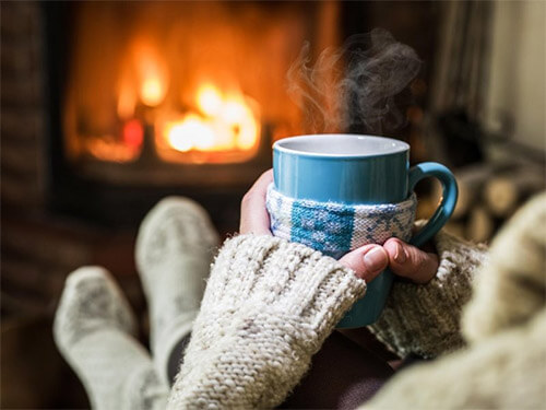 Woman in front of fireplace with warm tea and thick socks to warm cold hands and feet