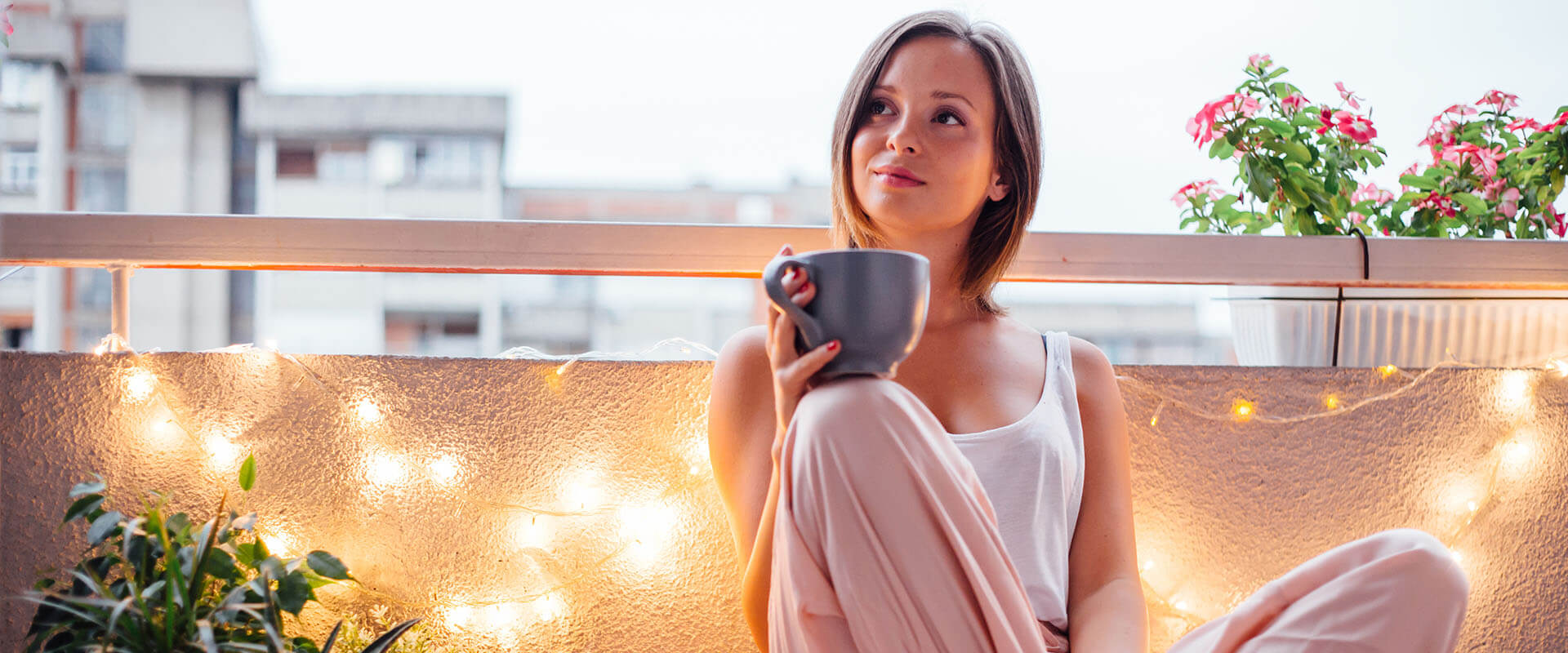 Happy woman on her balcony sitting on cushion drinking tea