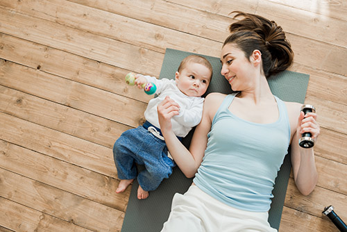 Mother is lying on the floor with baby and both are exercising with dumbbells