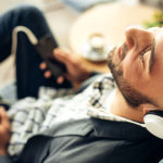 Man relaxing on sofa with headphones on cell phone to wellness music