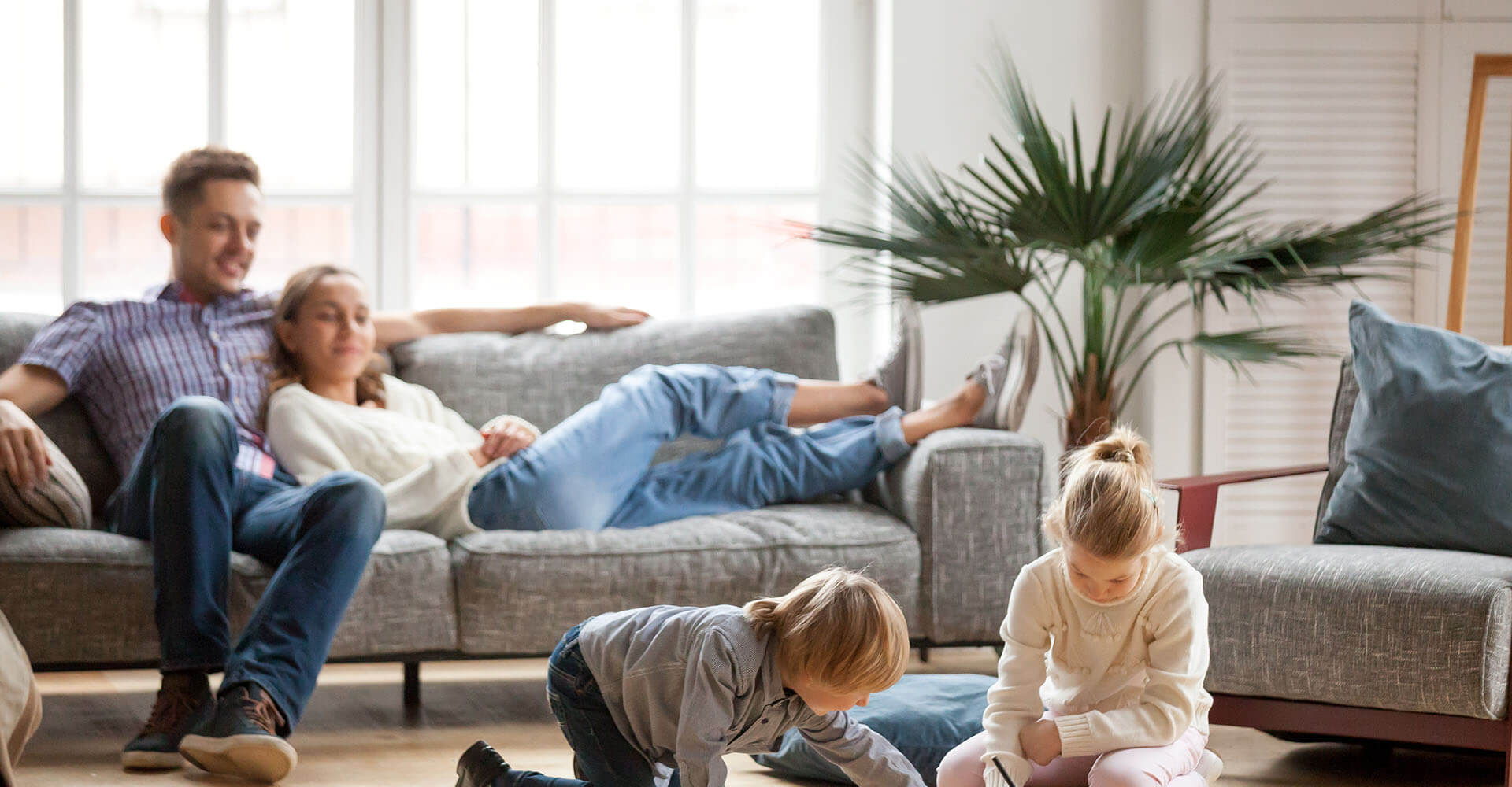 Family in the living room - the parents are sitting relaxed on the couch while the children are playing exuberantly