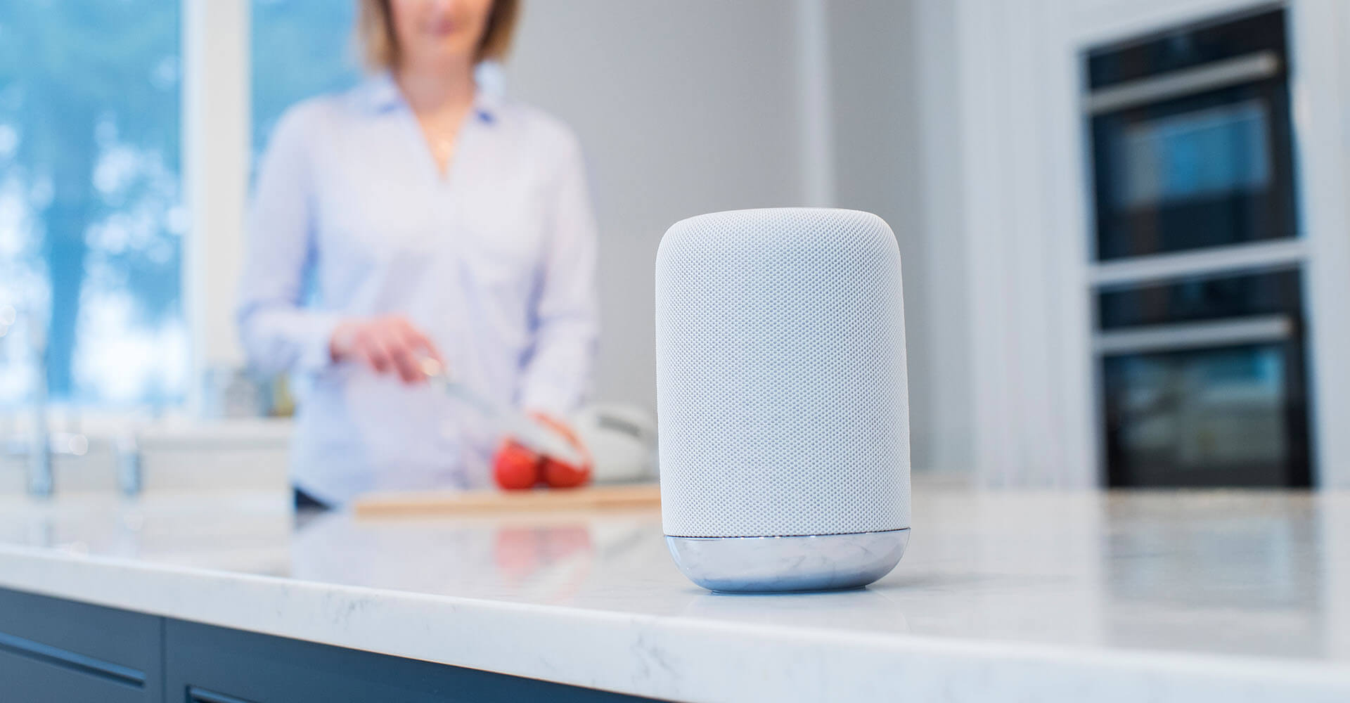 Woman in the kitchen in the background - in the foreground a smart speaker