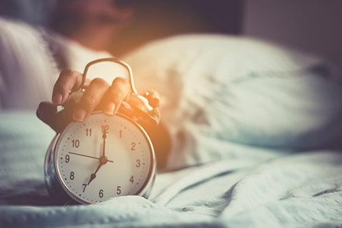 Woman with problems to fall asleep turns off the alarm clock in the morning
