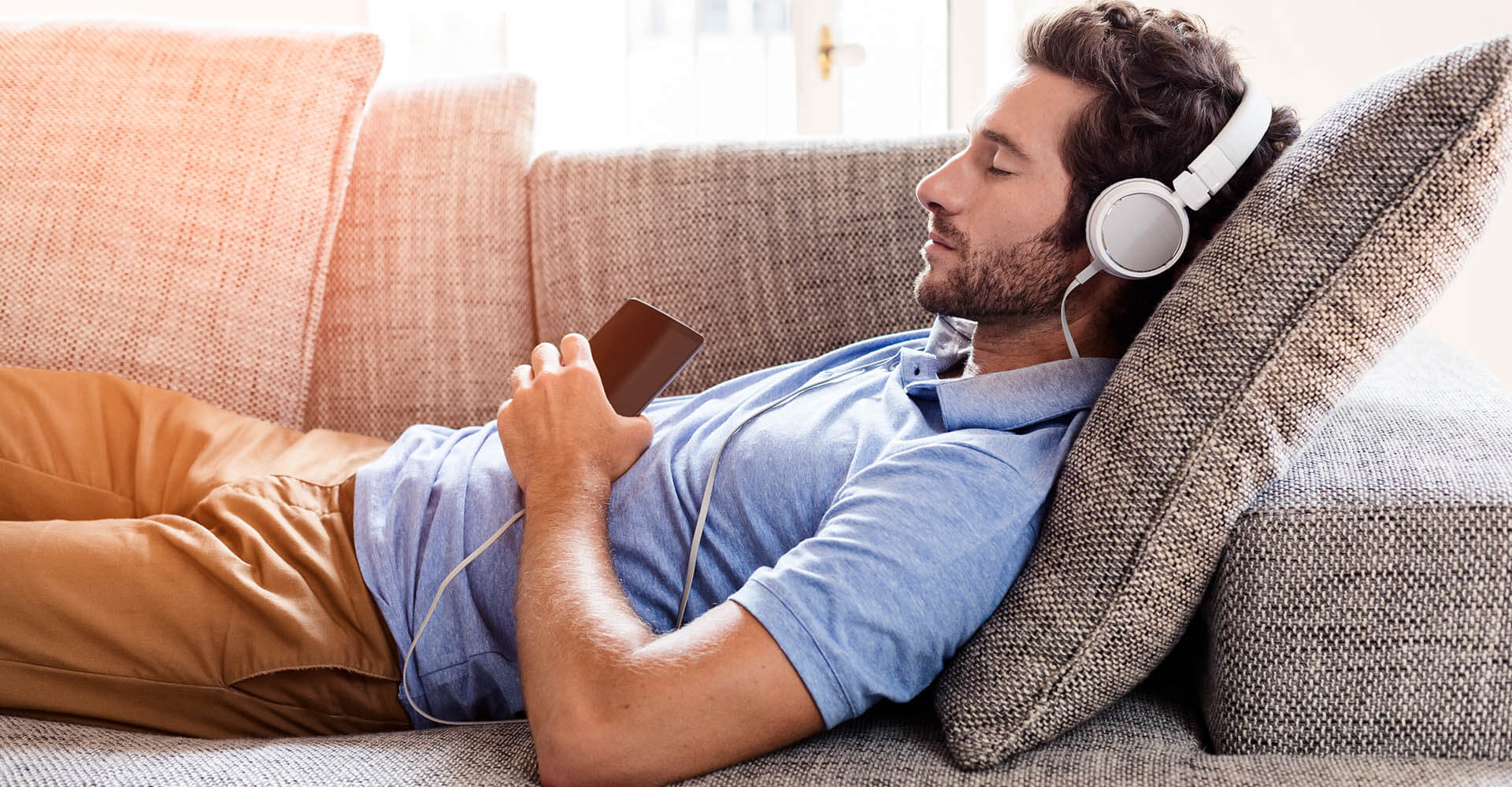 Man falling asleep on sofa while listening to music with headphones