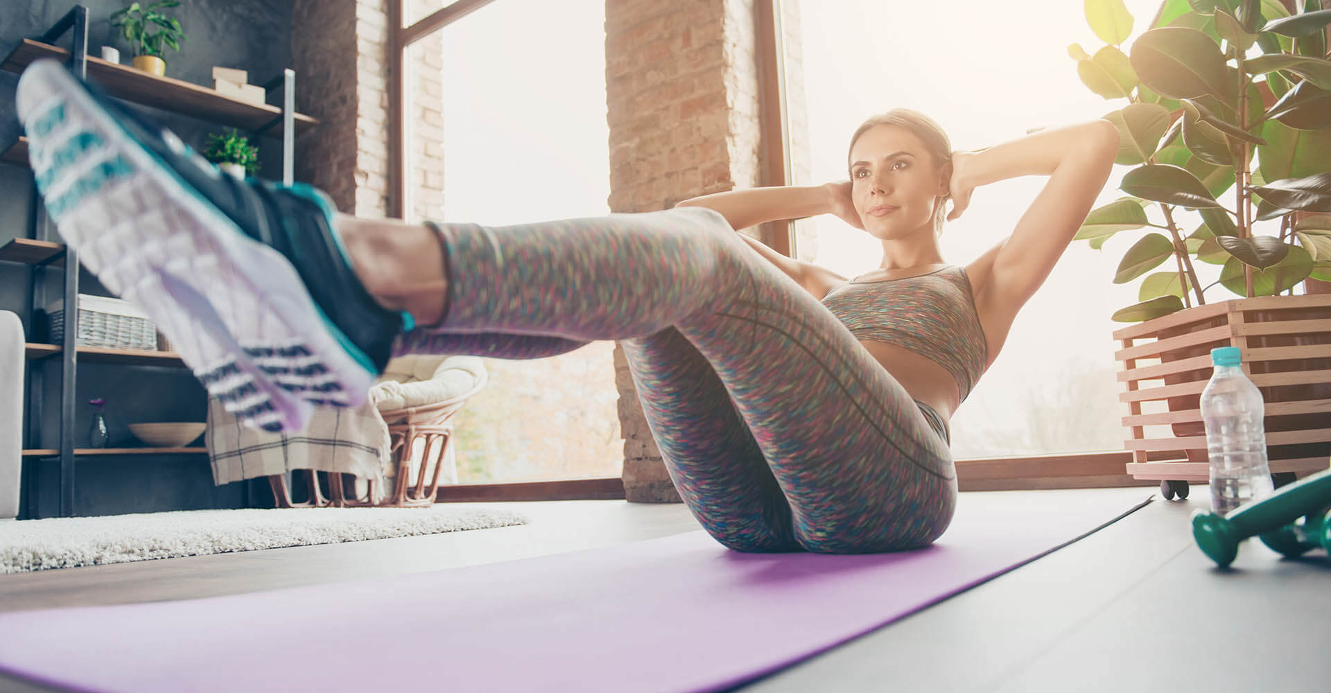 Woman doing sit-ups in living room on sleeping mat while listening to sports music