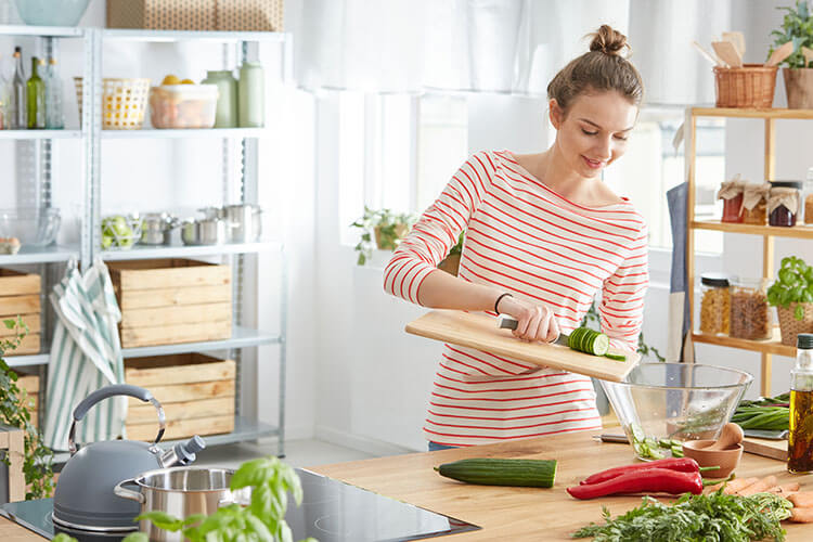 Young woman preparing healthy food from fruits and vegetables in kitchen