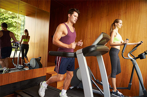 Man runs on treadmill while woman works out on cross trainer