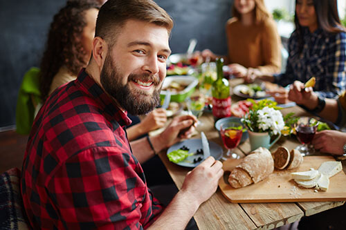 Man sitting smiling at lunch table with friends and eating