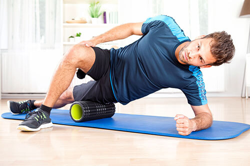 Man trains at home on mat and fascia roll