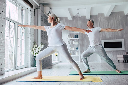 Elderly senior couple does yoga exercises at home