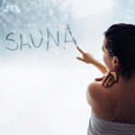 A woman writes the word "sauna" on a fogged window pane