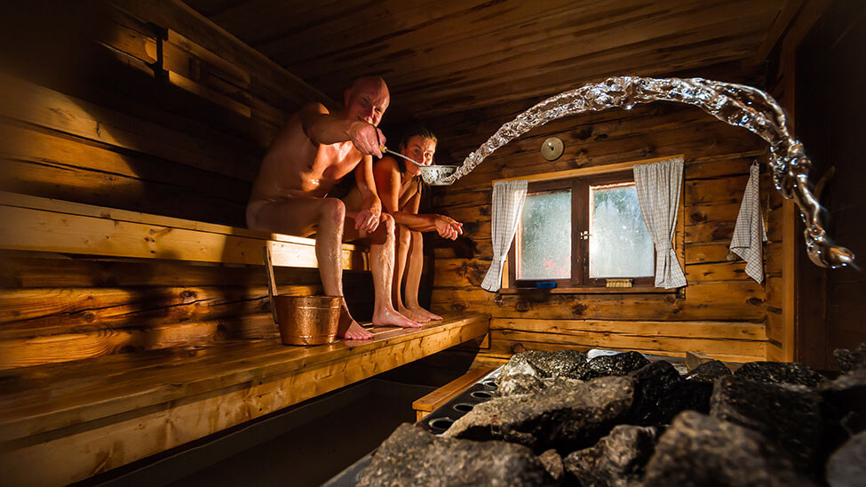 Couple in sauna relaxing with ladle pouring water on sauna charcoal