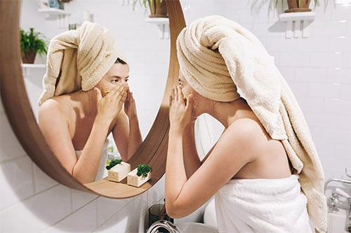Woman with face mask in front of mirror in bathroom