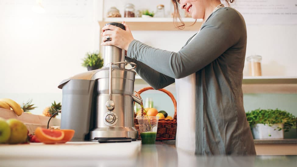 Woman using juicer in kitchen for green juice