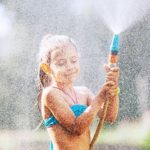 Girl cools off in summer in garden with water hose