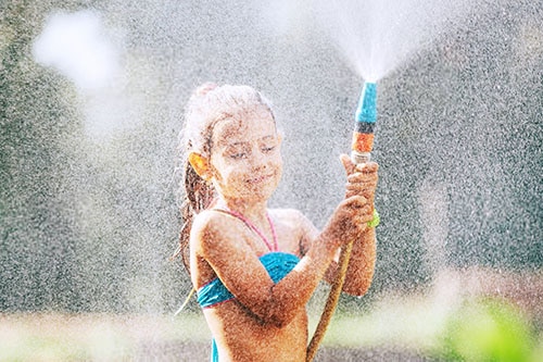 Girl cools off in summer in garden with water hose