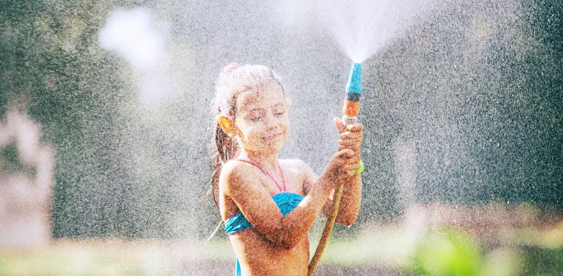 Girl cools off in summer in garden with water hose