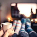 Couple at movie night with wool socks and cup of tea in front of television set