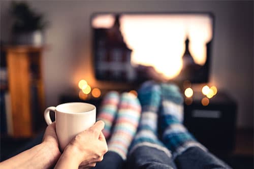 Couple at movie night with wool socks and cup of tea in front of television set