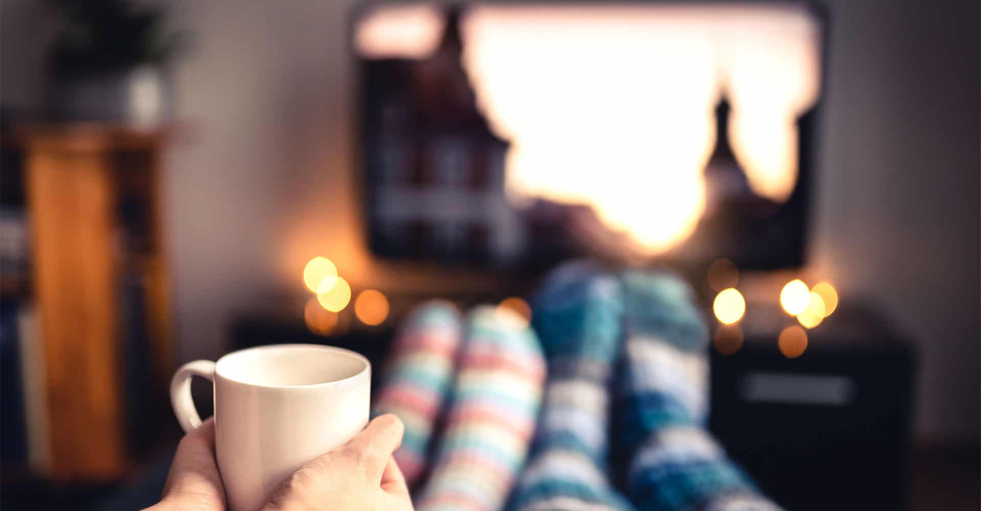 Couple at movie night with wool socks and cup of tea in front of television set