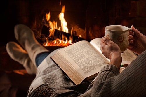 Man taking a break with a book and tea by the fireplace