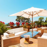 Sonnige Luxus-Terrasse mit weißen Möbeln und einem weißen Sonnenschirm