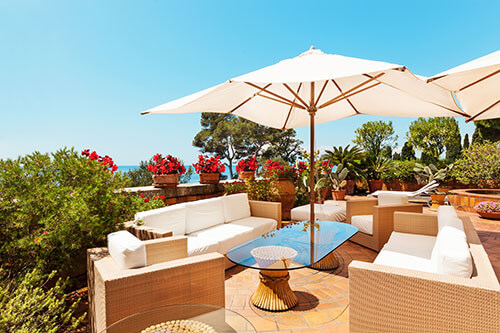 Sonnige Luxus-Terrasse mit weißen Möbeln und einem weißen Sonnenschirm