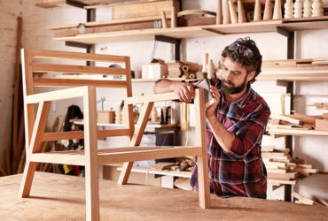 DiY-Heimwerker, der in Garage oder Werkstatt einen Holzstuhl schleift