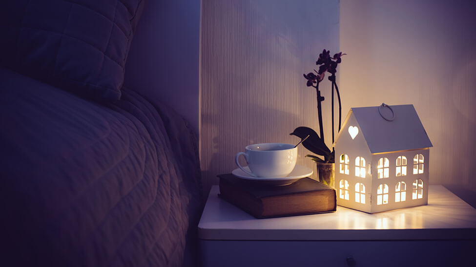 Buch, Tasse Tee und Kerzen neben dem Bett