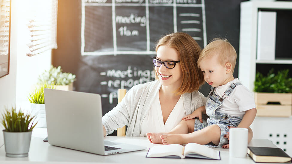 Mutter arbeitet am Laptop mit Baby auf Schreibtisch