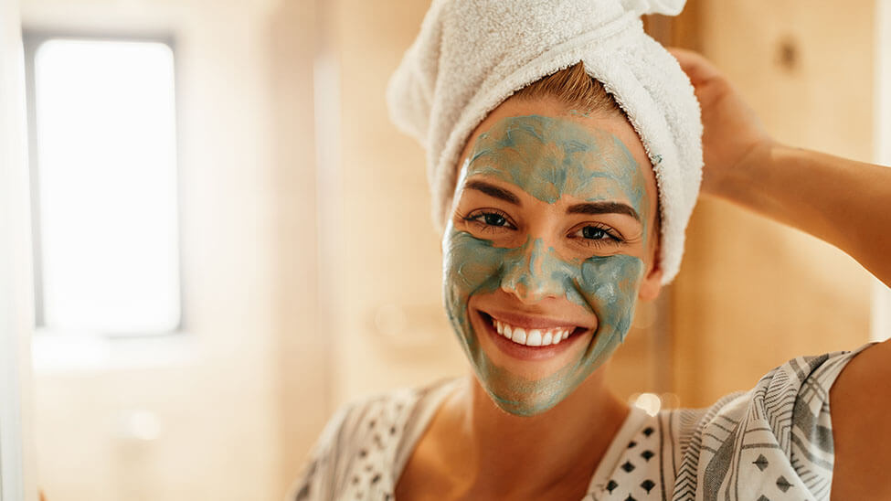 Frau macht Wellnesstag und lächelt mit Gesichtsmaske im Bad