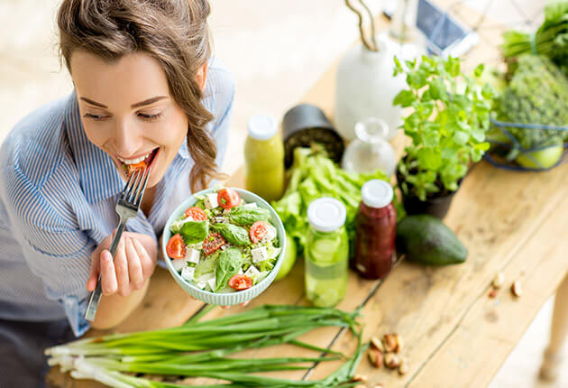Frau isst einen Salat, auf dem Tisch steht allerlei Gemüse