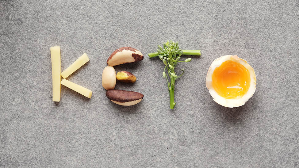 Der Begriff Keto dargestellt durch Kartoffel-Sticks, Nüsse, Grünzeug und ein Ei