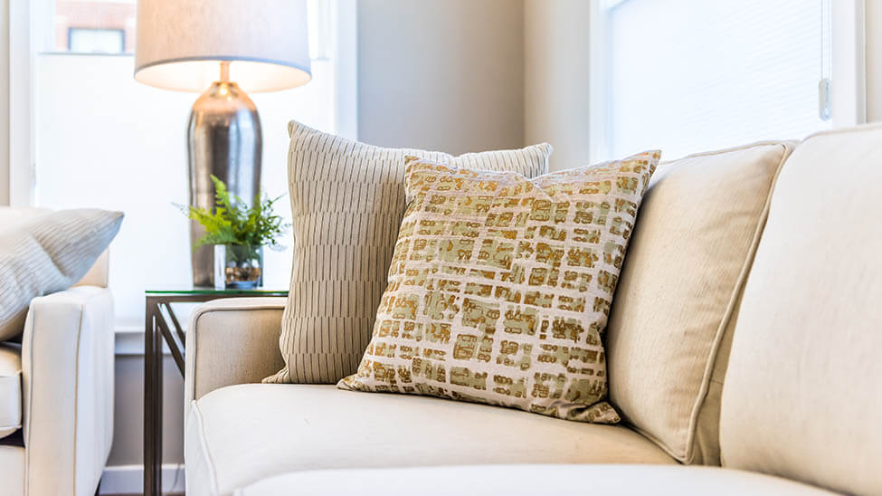 Cremefarbene Wohnzimmer-Couch mit verschiedenen Kissen und einer Lampe im Hintergrund