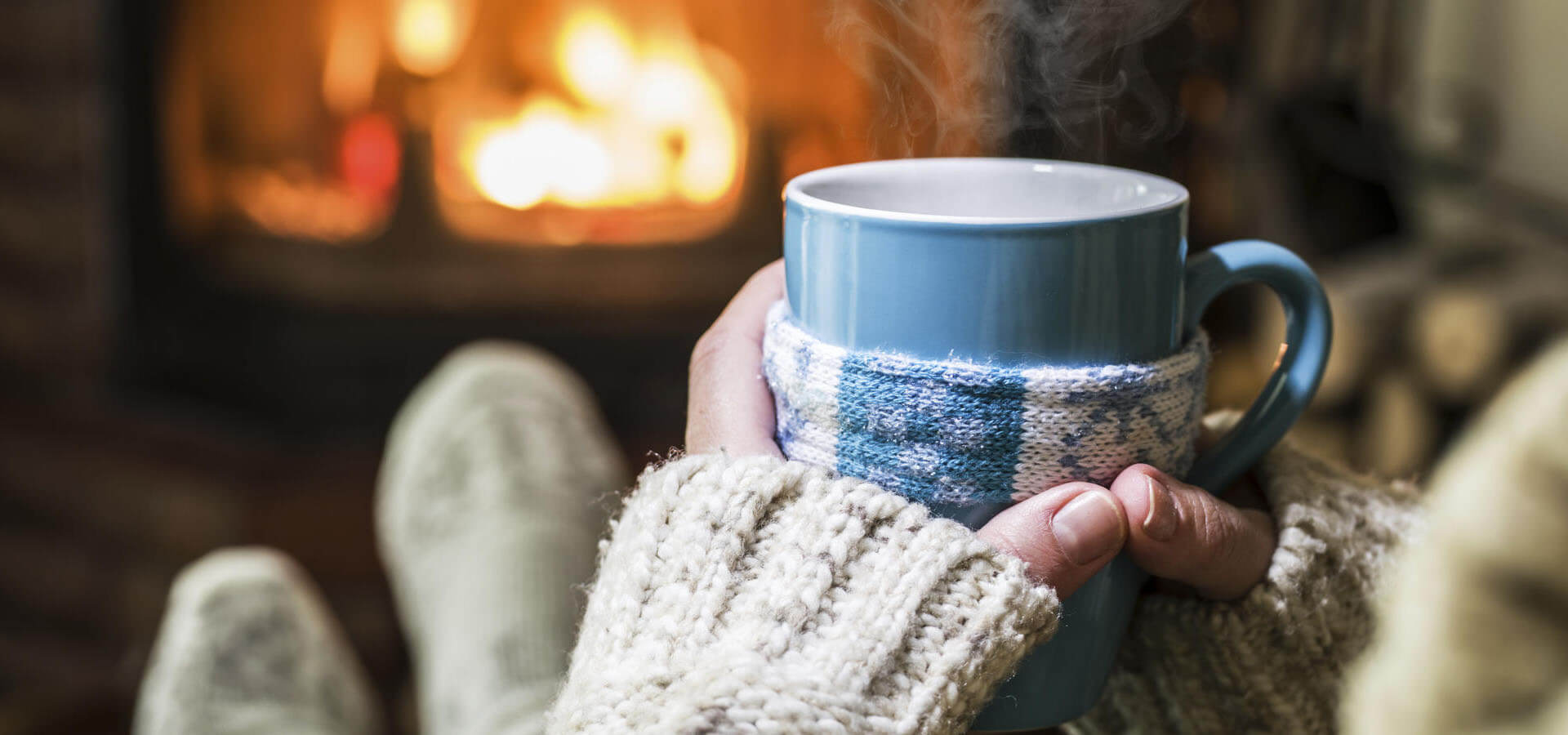 Frau vor Kamin mit warmen Tee und dicken Socken, um kalte Hände und Füße zu wärmen