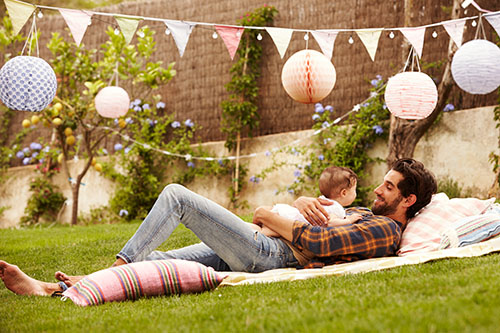 Vater liegt mit Baby auf dem Bauch im Garten auf einer gemütlichen Decke