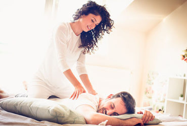 Frau gibt ihrem Partner auf gemeinsamen Bett eine Massage