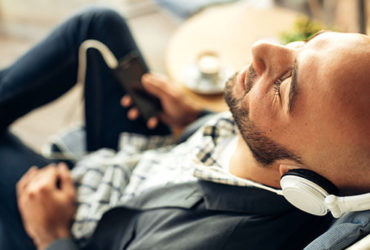Mann entspannt auf Sofa mit Kopfhörern am Handy zu Wellness Musik