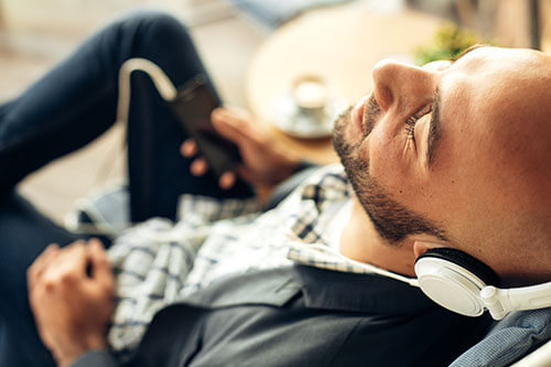 Mann entspannt auf Sofa mit Kopfhörern am Handy zu Wellness Musik