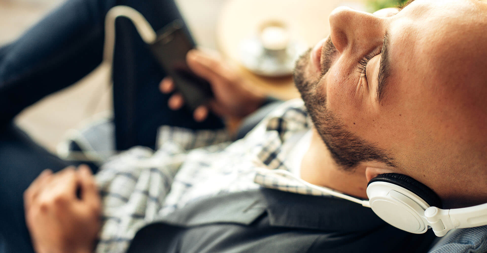 Mann entspannt auf Sofa mit Kopfhörern am Handy zu Wellness Musik