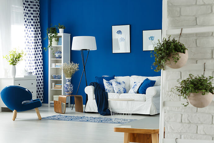 Blau und weiß gehaltenes Wohnzimmer mit Sessel, Couch, Regal und blauer Wand