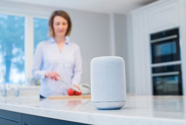 Frau in der Küche im Hintergrund - im Vordergrund ein Smart Speaker