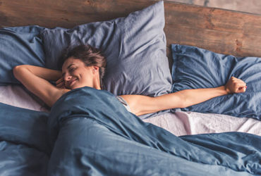 Junge Frau streckt sich glücklich im Bett nach Aufwachen