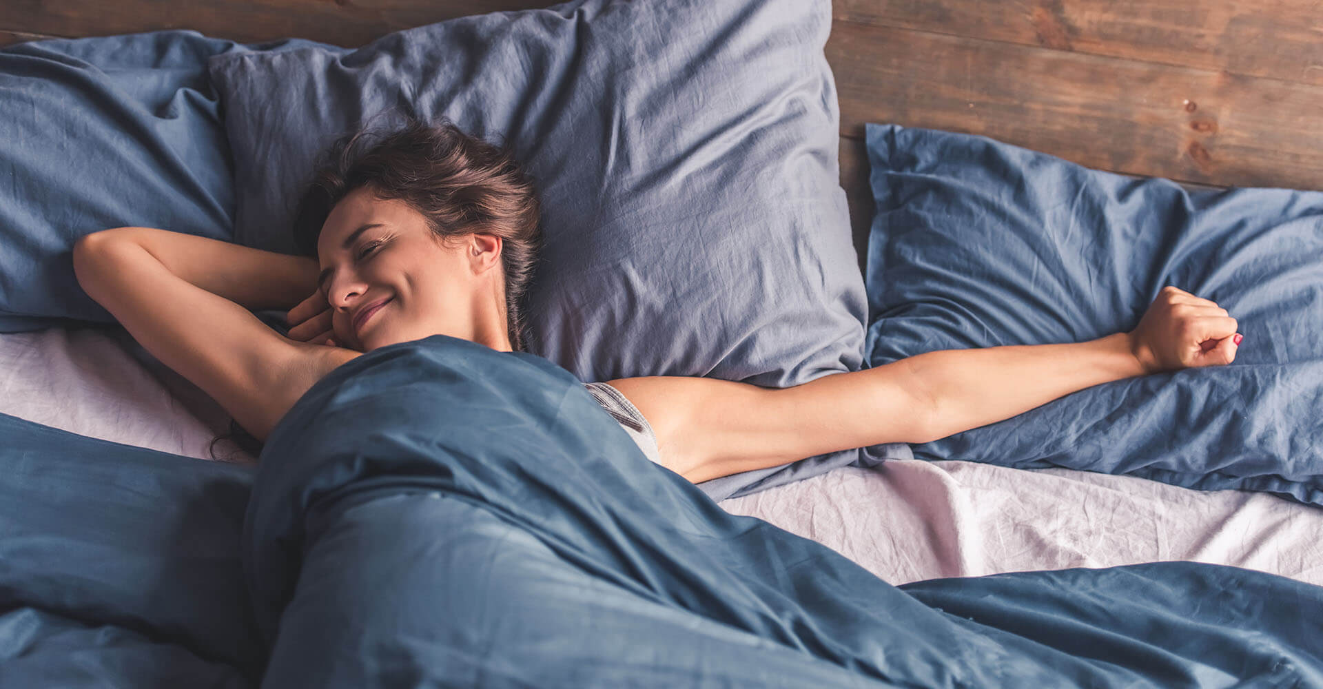 Junge Frau streckt sich glücklich im Bett nach Aufwachen